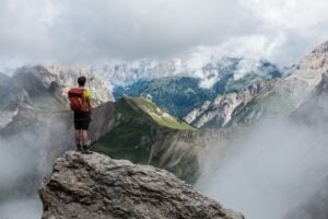 man wearing yellow t-shirt standing on cliff facing mountain
