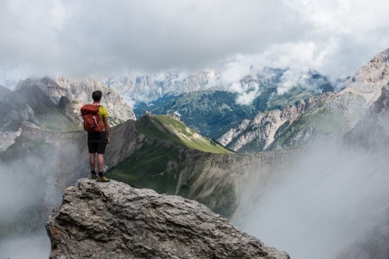 man wearing yellow t-shirt standing on cliff facing mountain